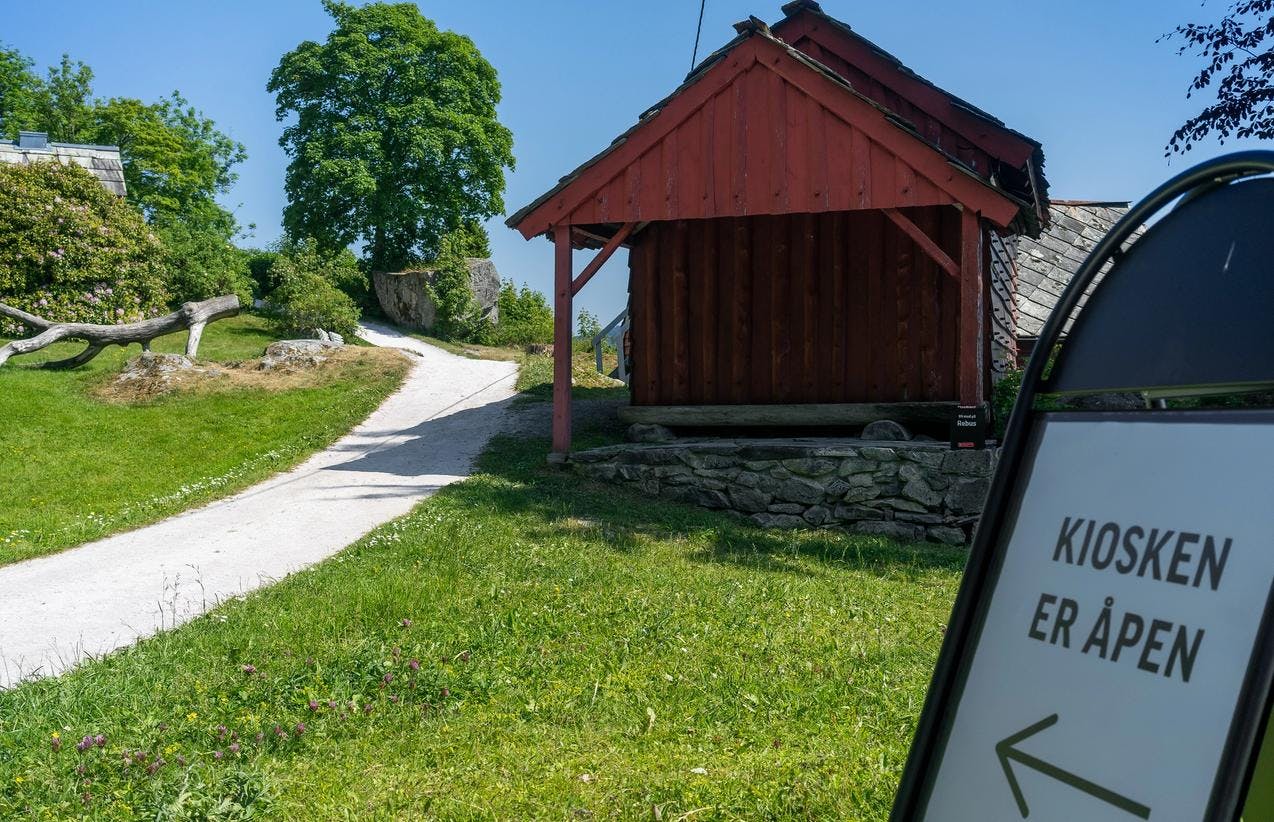 Røde hus langs en sti, og et skilt som peker til venstre med skriften kiosken er åpen