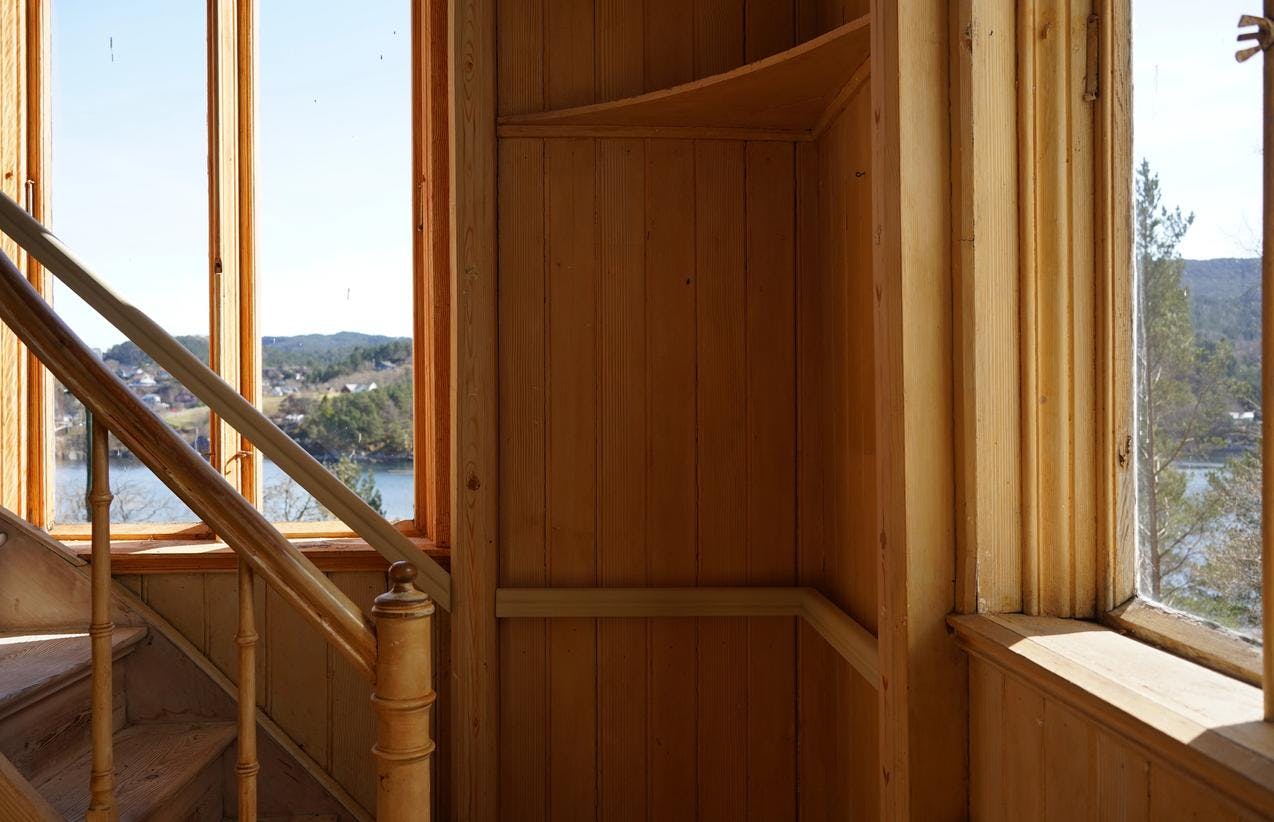 Fra trappehuset på Lysøen, med brune vegger og vinduer med utsikt mot sjø og trær