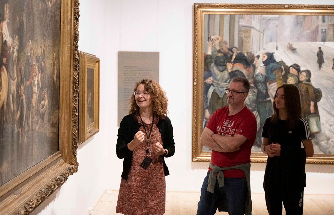 Foto av en formidler sammen med to personer, foran et stort maleri
