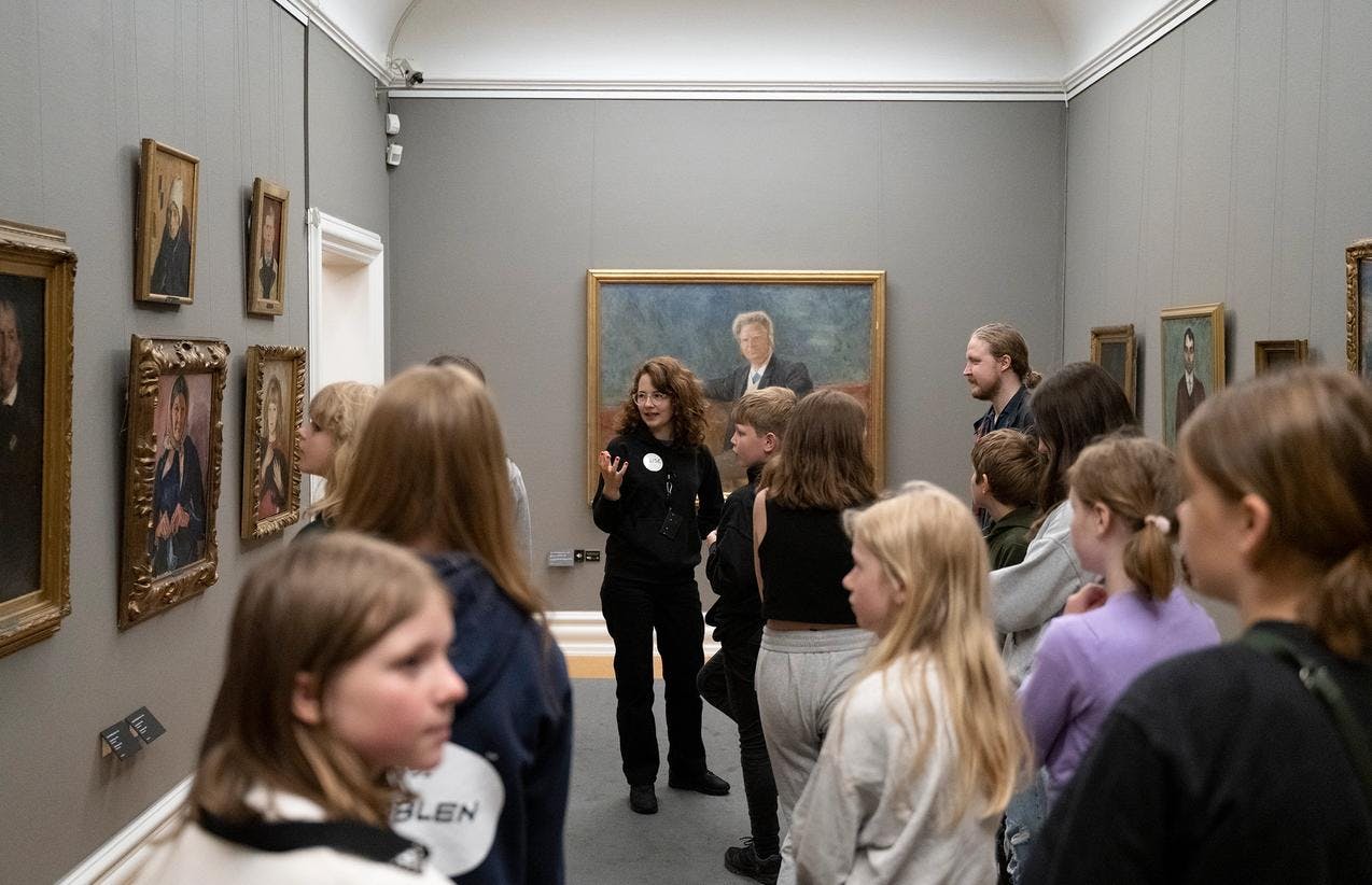 En kvinnelig guide viser en gruppe mennesker rundt i utstillingen i Rasmus Meyers samlinger.