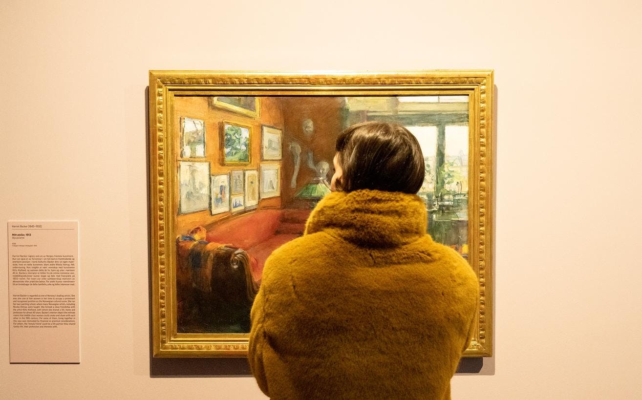 En person står foran et maleri av Harriet Backer, som henger på en vegg i en dus gul farge