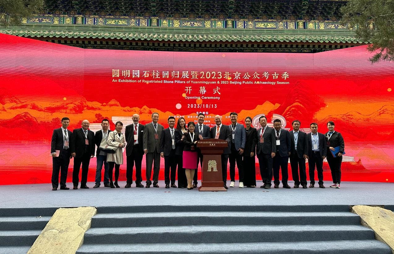 En gruppe mennesker på et podium foran en rød bakgrunn med kinesisk påskrift.